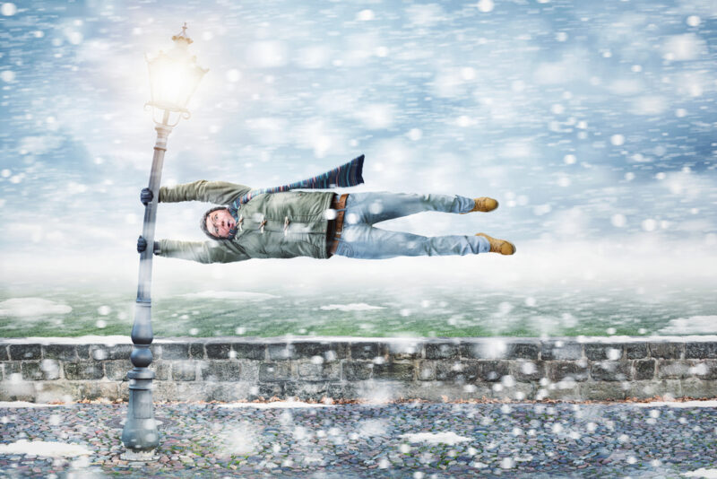 Funny picture of man getting blown sideways by winter storn holding on to street pole - cheap home insurance in Washington